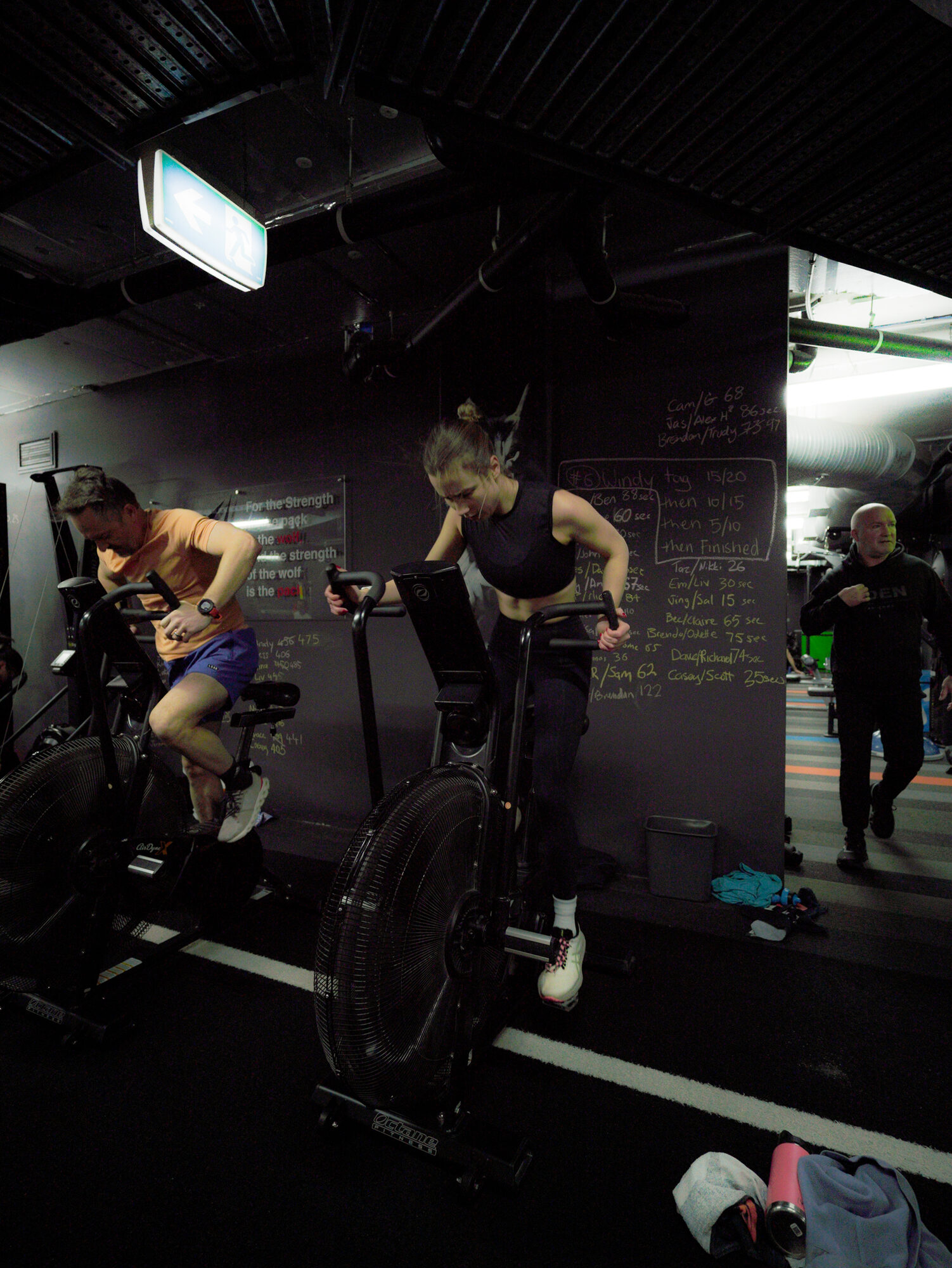 Members on the air bikes with the session board chalked up behind them